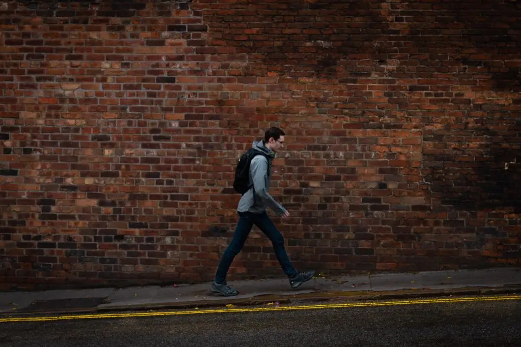 Picture of a young person wearing a backpack walking uphill next to a road